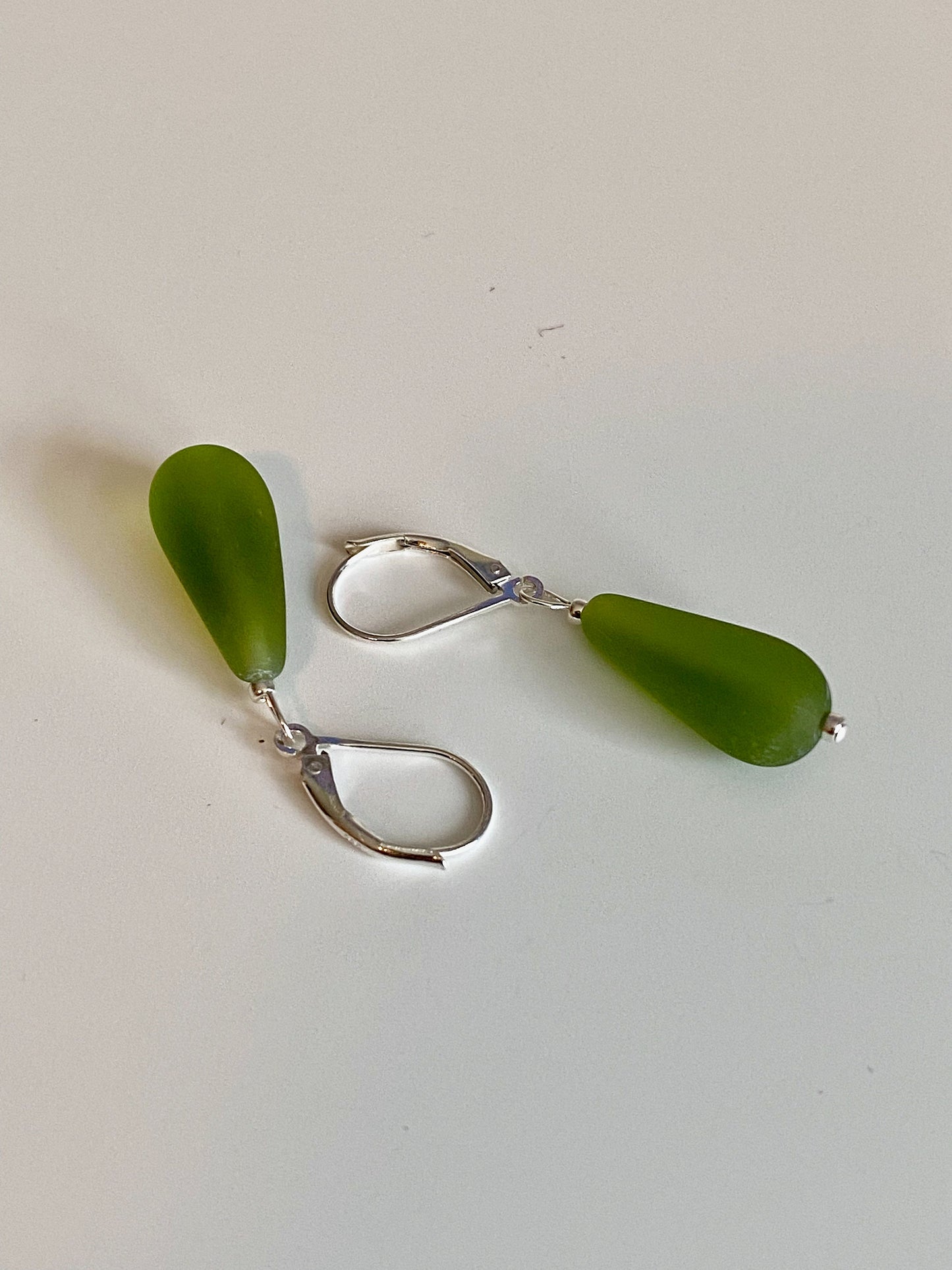 Soft sea glass type frosted olive green color teardrop earrings. Fashioned with a quality sterling silver lever back clasp.