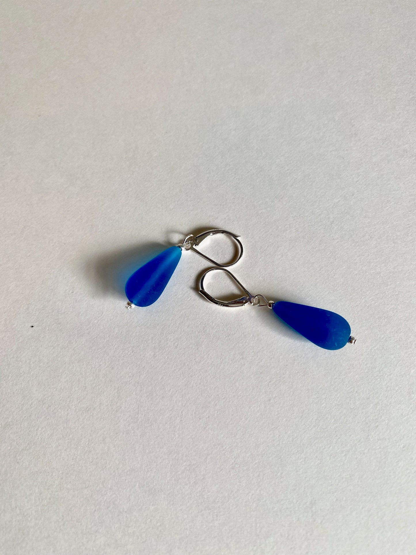 Soft sea glass type frosted capri blue color teardrop earrings. Fashioned with a quality sterling silver lever back clasp.